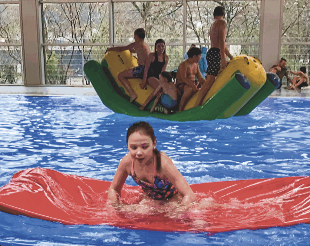 Kinder spielen auf einer aufblasbaren Wasserplattform in einem Hallenbad