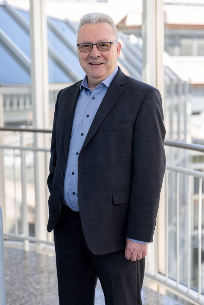 Peter Erb steht in einem Anzug vor einem modernen Glasgebäude.