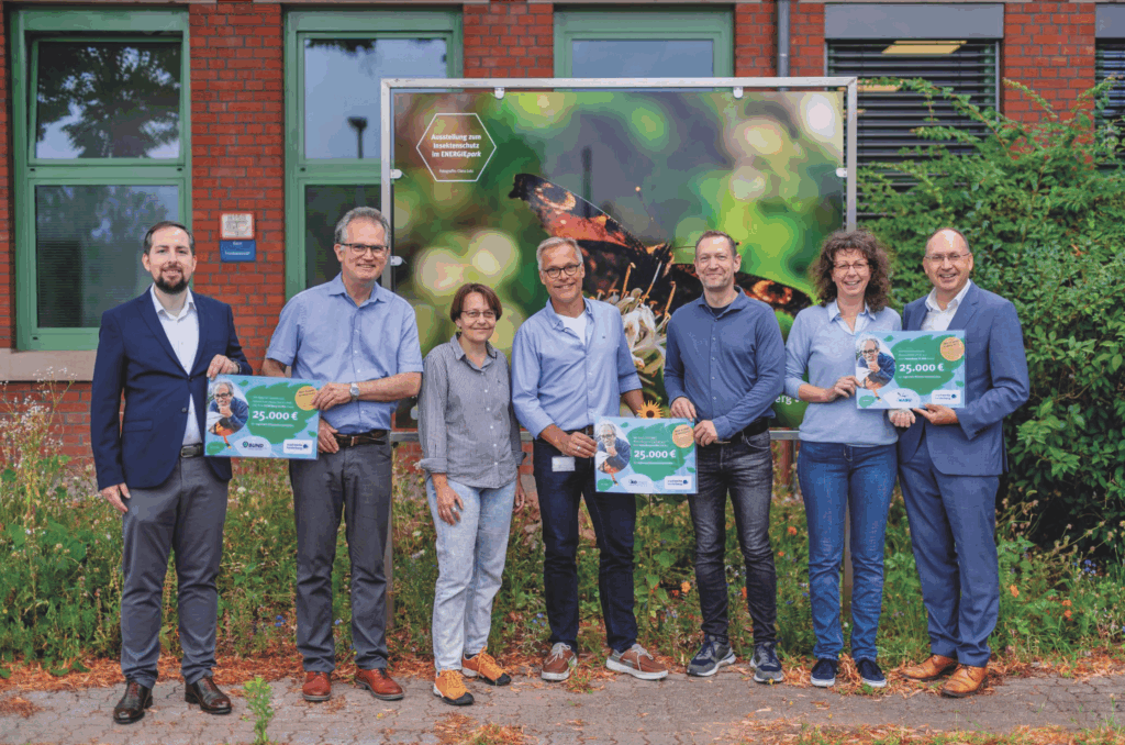 Sieben Personen stehen vor einem Banner mit einem Schmetterling und halten Schecks über 25.000 Euro für den Klimaschutzfonds Partnerverbände