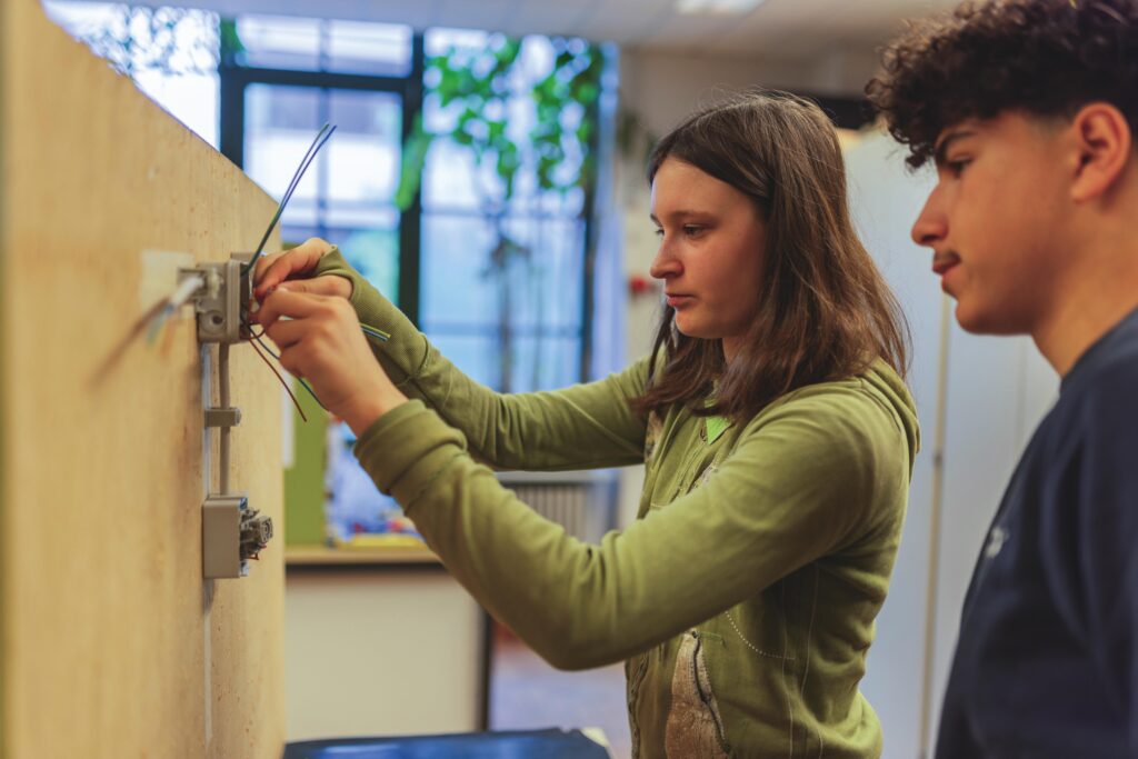 Junges Mädchen arbeitet an einer elektrischen Installation während des Girls' Day 2024, begleitet von einem männlichen Betreuer