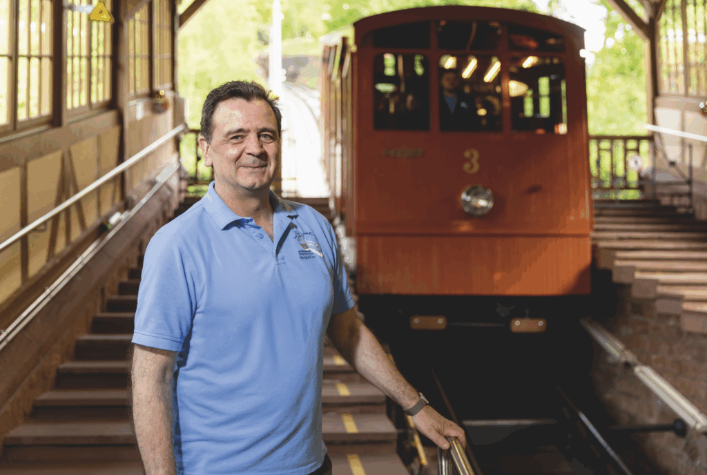 Martin Wenger, Wagenbegleiter bei den Heidelberger Bergbahnen, steht in blauer Polo vor der Bergbahn Nummer 3 in der Station