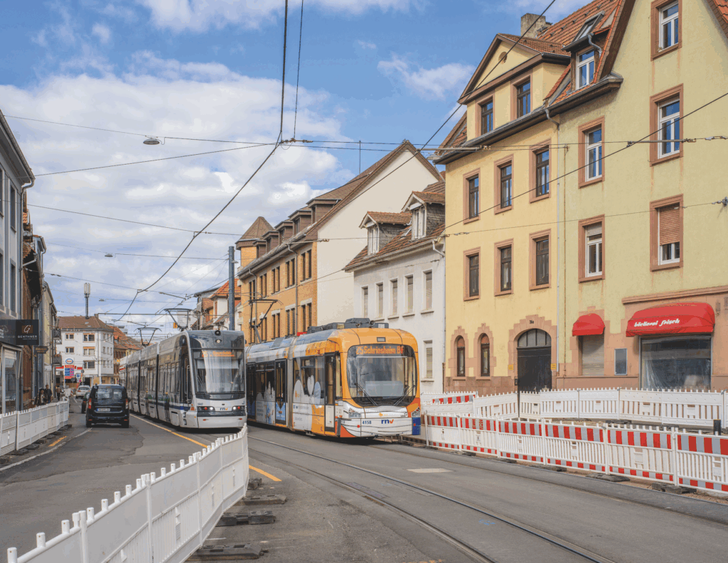Zwei Straßenbahnen auf Gleisen in einer Stadtstraße mit mehrstöckigen Gebäuden und Baustellenabsperrungen