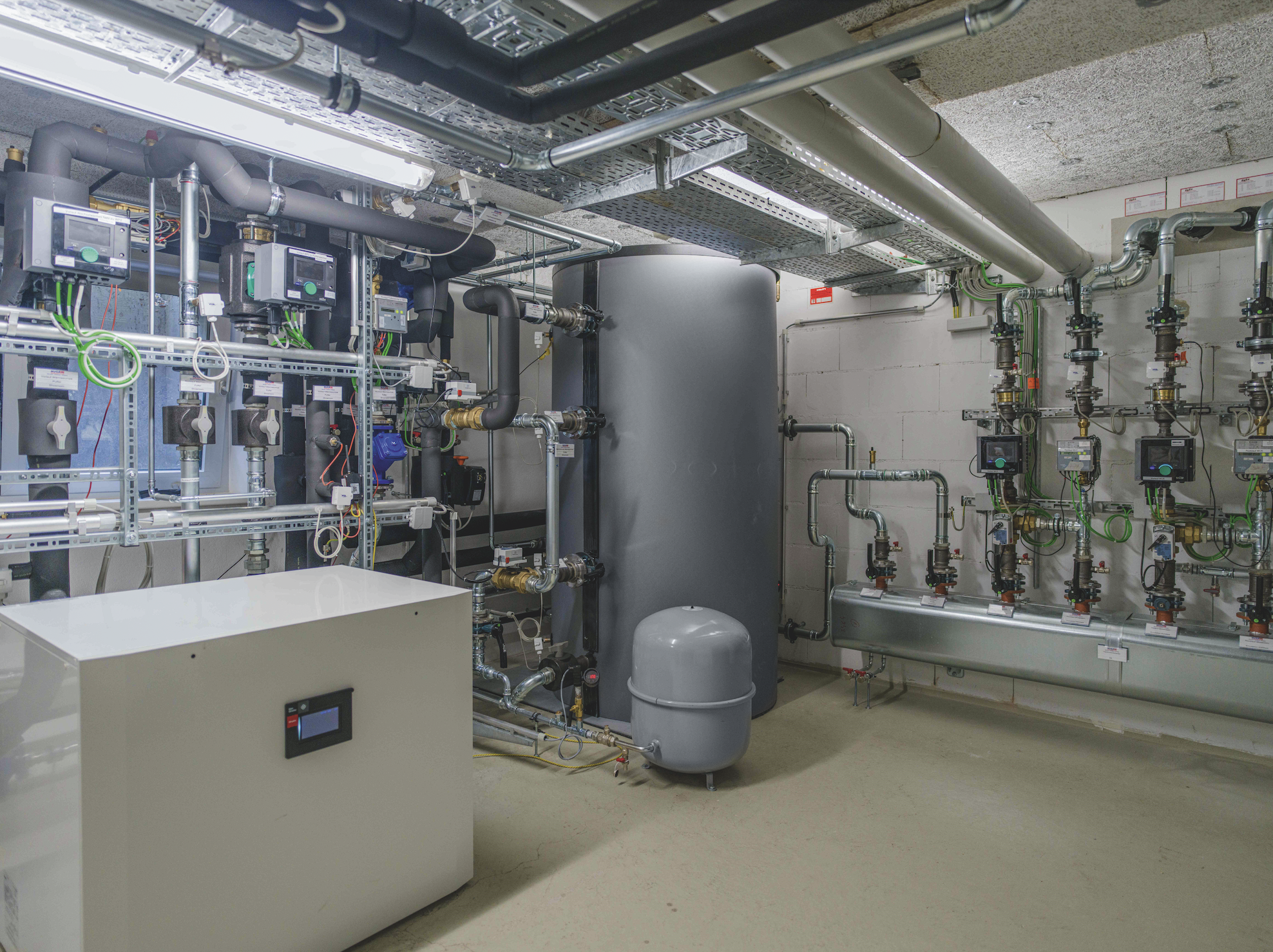 Technikraum mit großen grauen Tanks, Rohrleitungen und Steuergeräten an der Wand