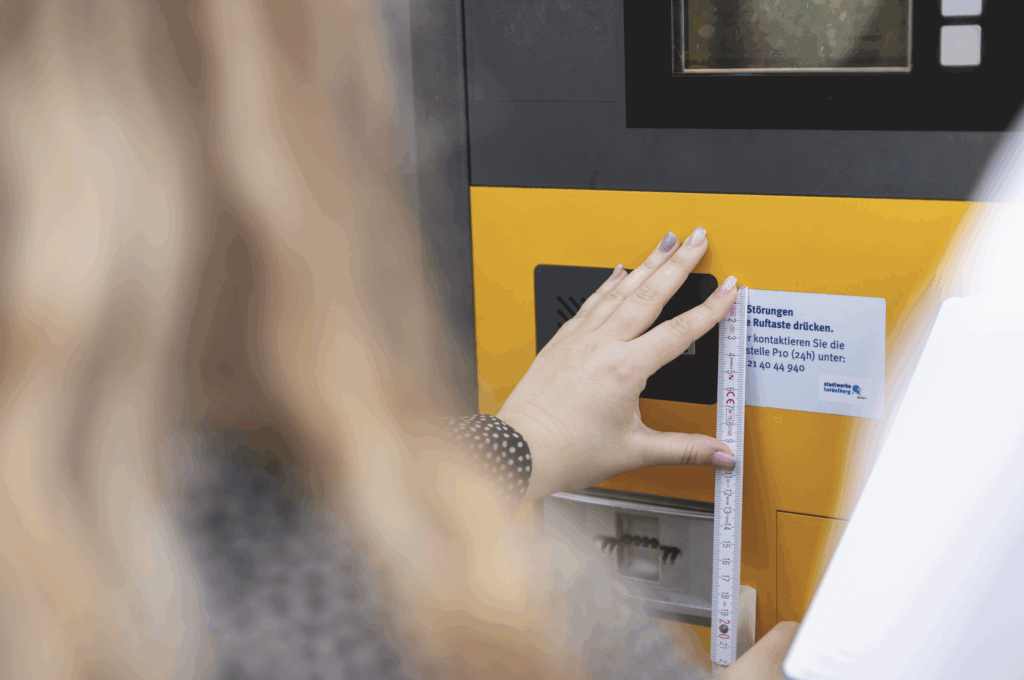 Sarah Buchwitz aus dem Marketing-Team misst mit einem Zollstock ein gelbes Parkautomatenbedienfeld