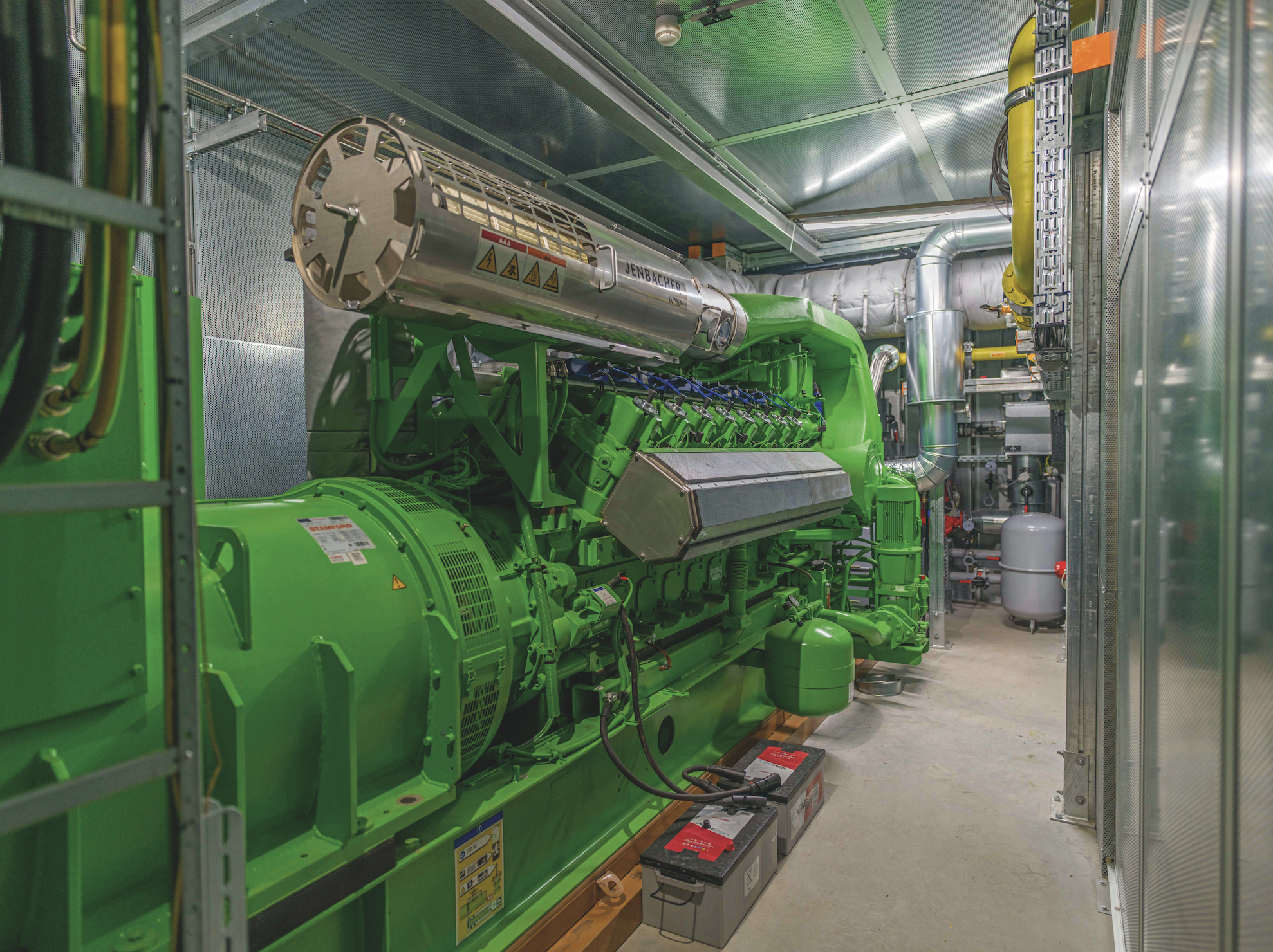 Große grüne Industriemaschine in einem Technikraum mit Metallrohren und Kabeln