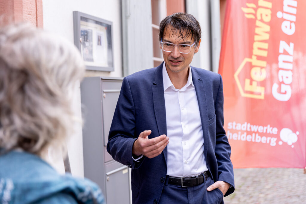 Thorsten Elfner spricht mit einer Frau in einem Innenhof, im Hintergrund ein rotes Banner