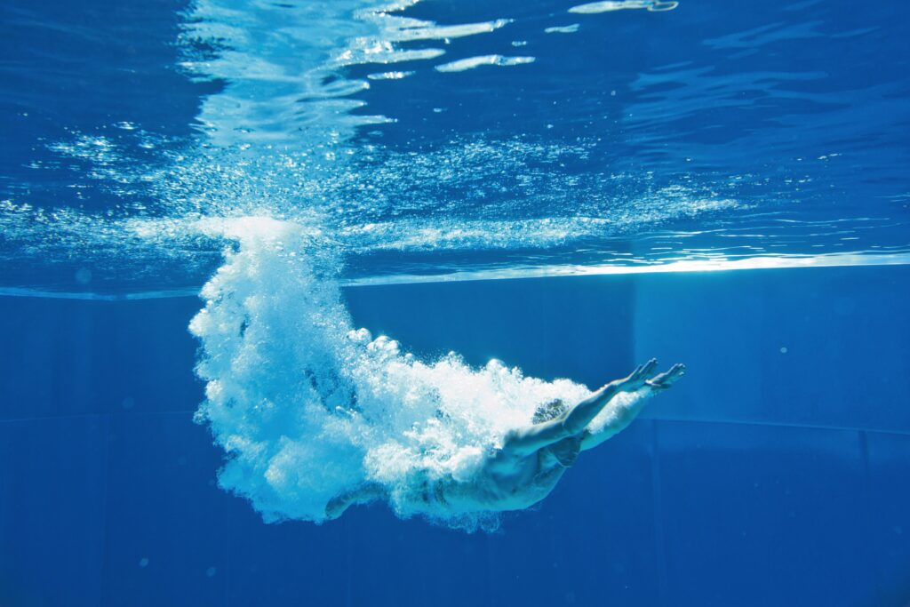 Person taucht kopfüber ins klares Wasser eines Schwimmbeckens